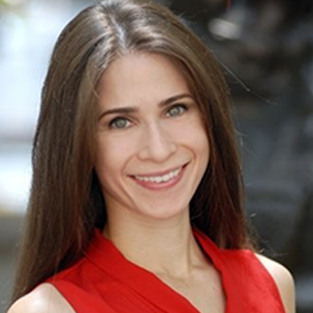 A woman with long brown straight hair in a red shirt smiling in front of an outdoor backdrop.